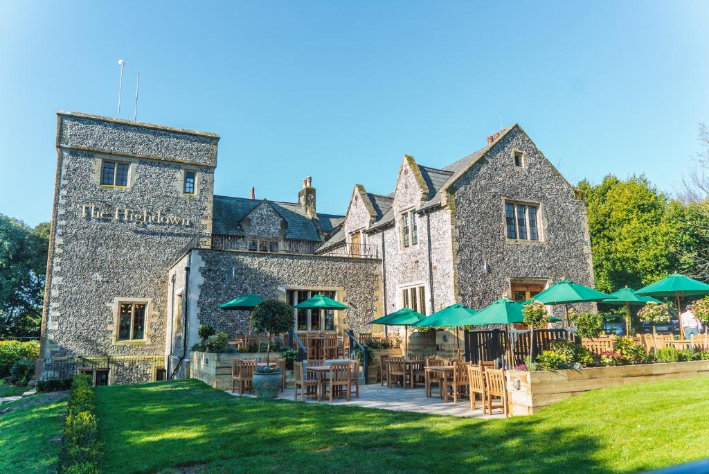 un grand bâtiment en pierre avec des tables et des parasols verts dans l'établissement The Highdown – Brunning and Price, à Worthing