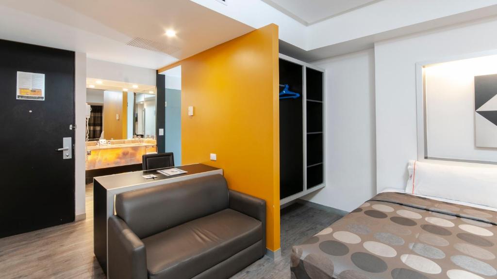 A compact guest room with a double bed, armchair, desk and open wardrobe.