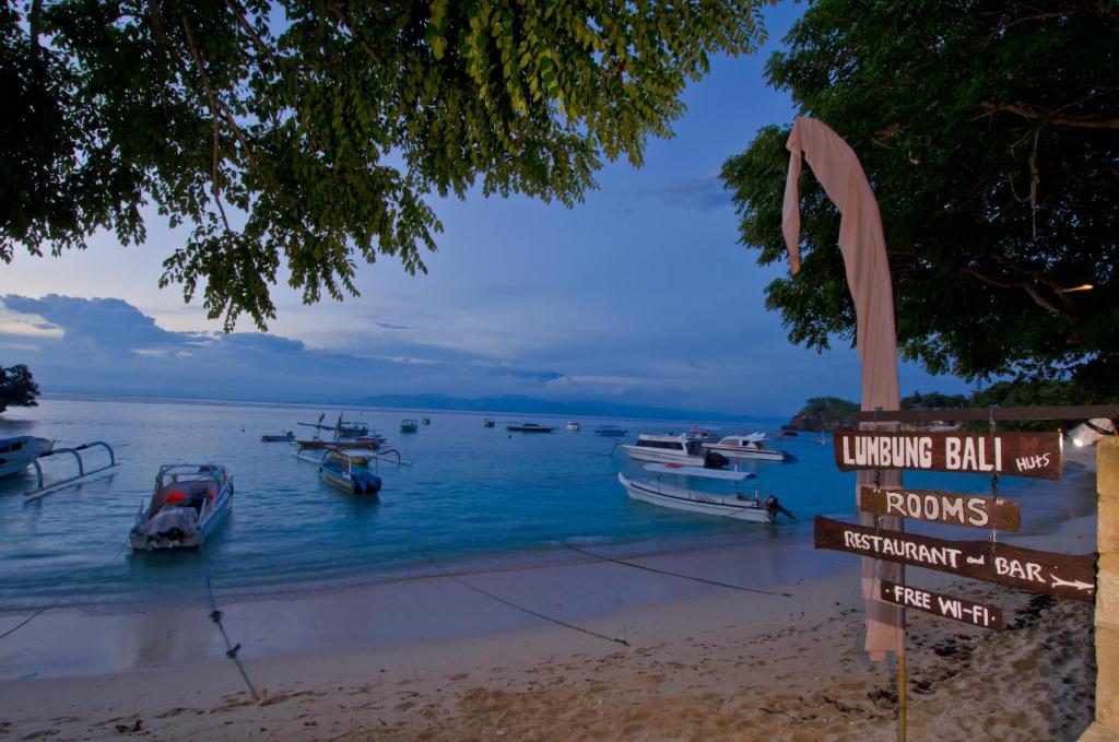 a sign on a beach with boats in the water at Lumbung Bali Huts in Nusa Lembongan