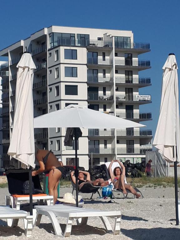 a group of people sitting on the beach with an umbrella at Complex Astoria mamaia nord in Mamaia Nord