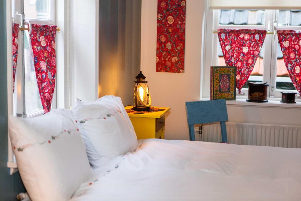 a bed with white sheets and pillows in a room with windows at Bed and Breakfast De Pepersteeg in Marken