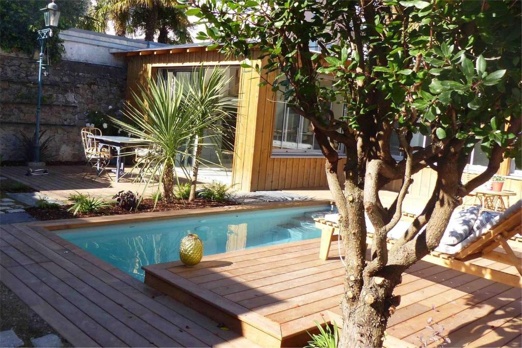 una piscina con terraza de madera junto a un árbol en Le Nid du Héron, gîte urbain avec piscine chauffée en Nantes