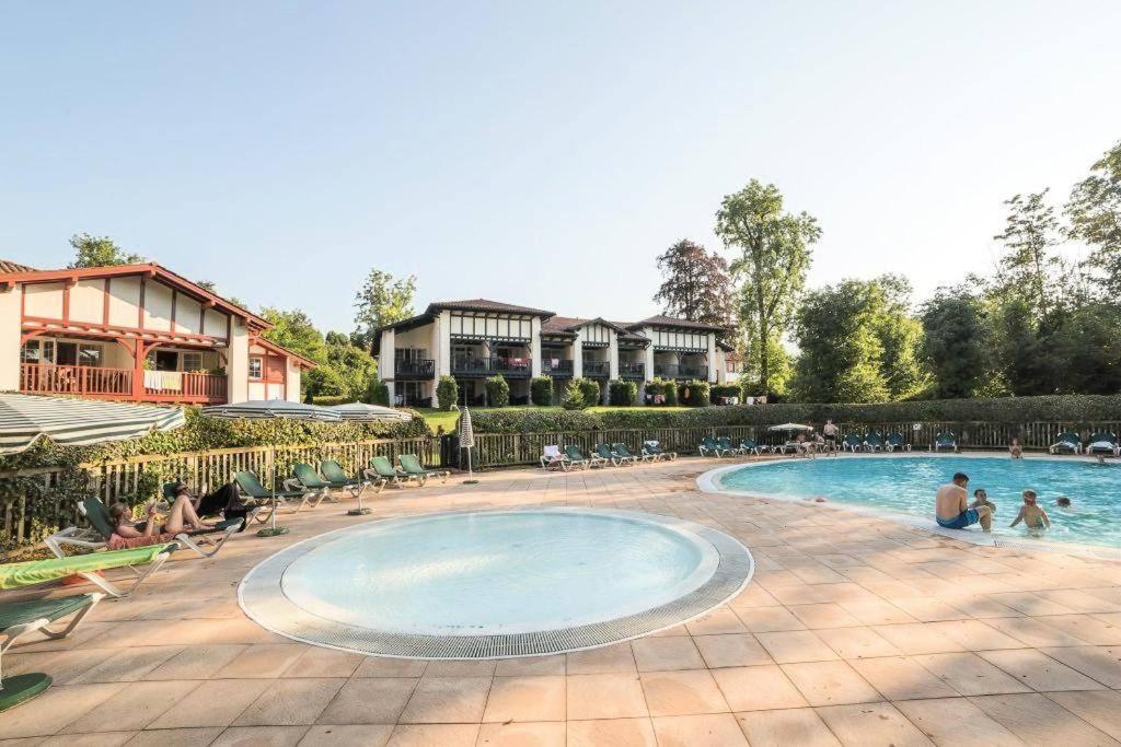 uma piscina num resort com pessoas sentadas à sua volta em Residence Parc Arradoy em Saint-Jean-Pied-de-Port