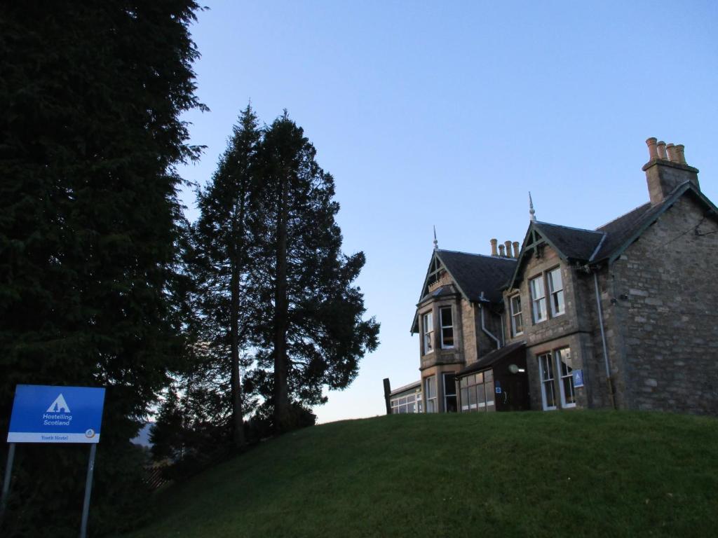 uma casa numa colina com um sinal em frente em Pitlochry Youth Hostel em Pitlochry