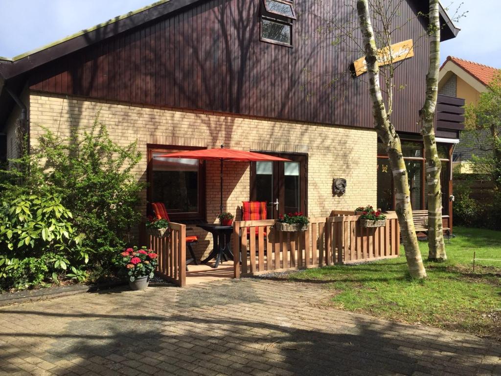 a woman sitting under an umbrella outside of a house at De Vier Berken 2 in De Koog