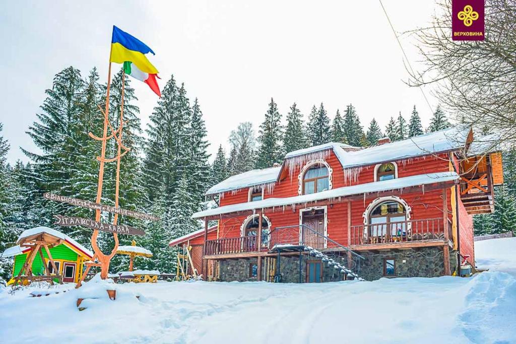 une grande maison en bois dans la neige avec un drapeau dans l'établissement Kitica house, à Verkhovyna