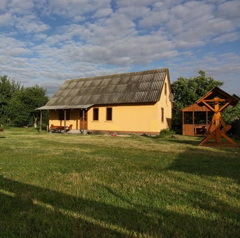 a yellow house with a gambrel roof in a field at Затока in Svityazʼ