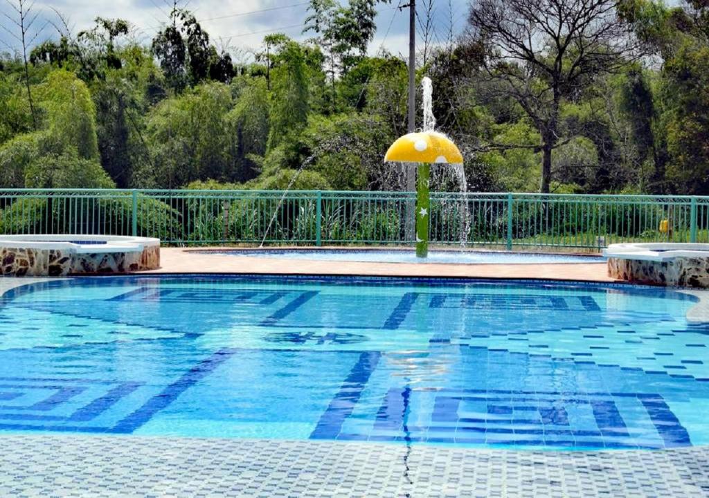 a swimming pool with an umbrella and a fountain at Hotel Campestre Paraiso Cafetero in Montenegro