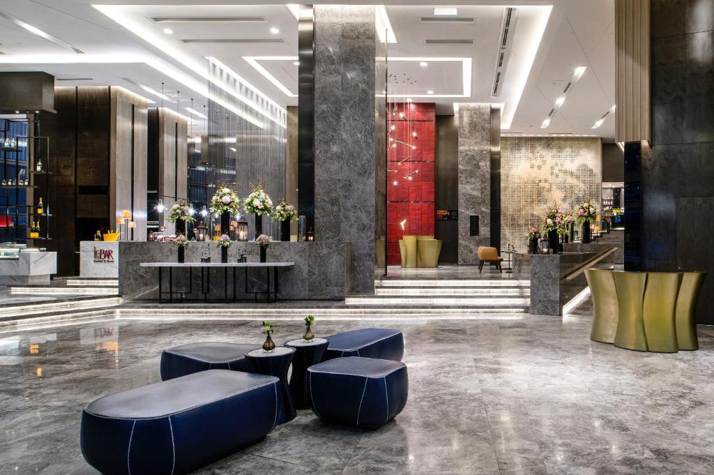 A polished hotel lobby with marble finishes, blue lounge stools, and flower arrangements.
