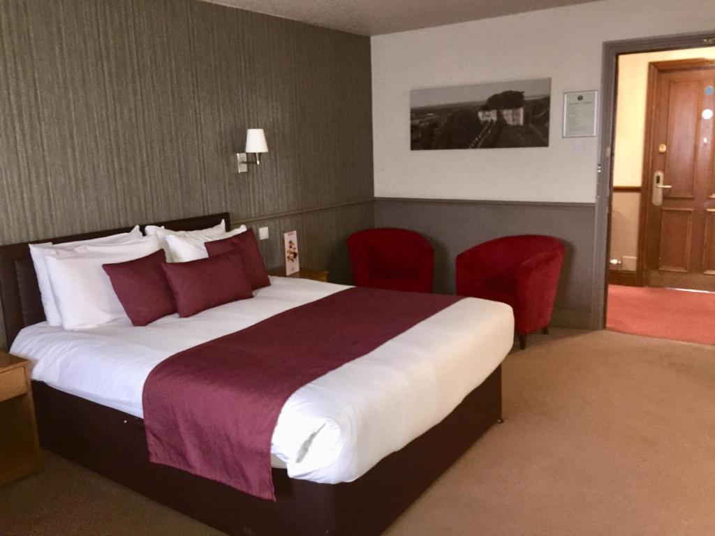 a hotel room with a large bed and red chairs at Windmill Farm Lincoln by Greene King Inns in Lincoln