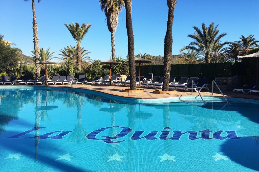 a large swimming pool with palm trees and a hotel sign at La Quinta at La Manga Club in La Manga del Mar Menor