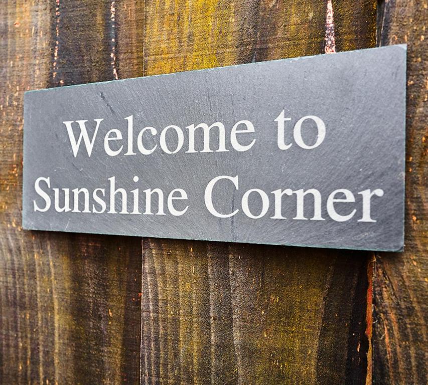 un panneau indiquant « Bienvenue au coin soleil sur une clôture en bois » dans l'établissement Sunshine Corner, à West Mersea