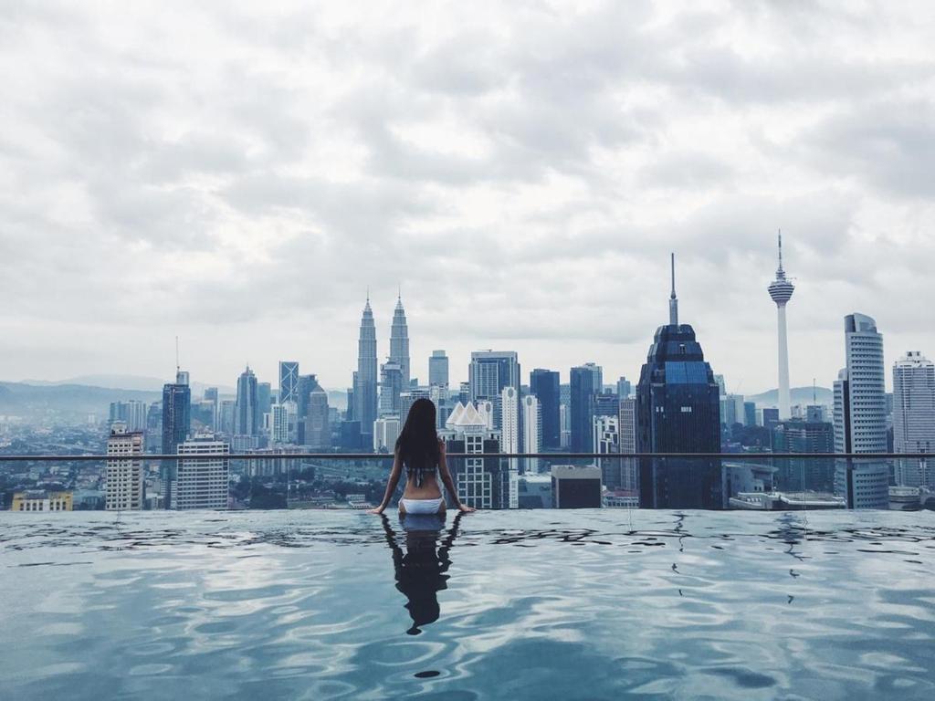 a woman sitting in a infinity pool overlooking a city at KLCC Inifinity Pool - The Regalia Residences & Suites by KL minsu in Kuala Lumpur