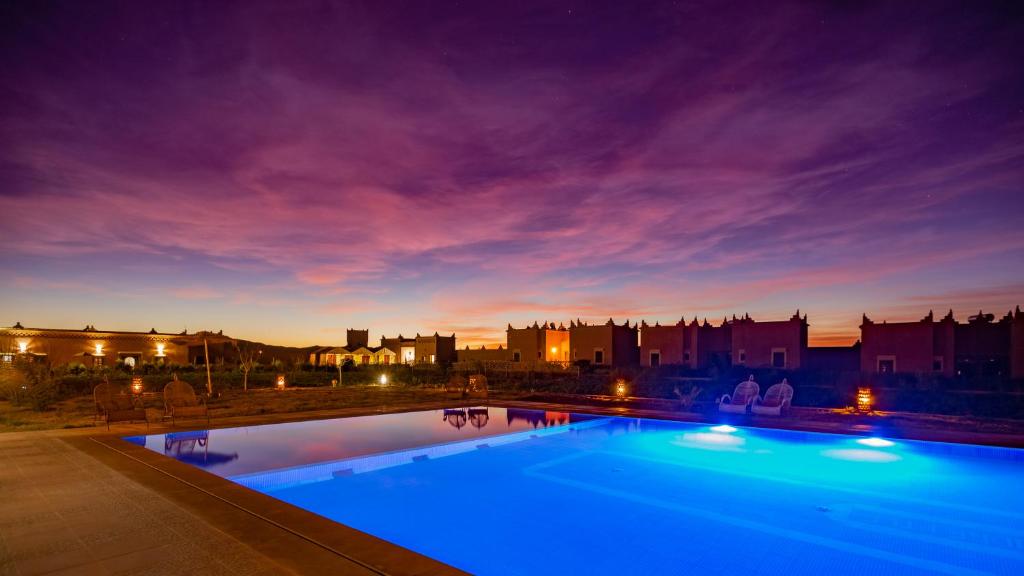 a swimming pool at night with a city in the background at Ecolodge l'île de Ouarzazate in Ouarzazate