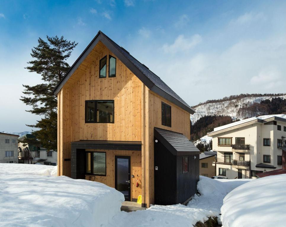 a house with a black roof in the snow at Harvest House Nozawa in Nozawa Onsen