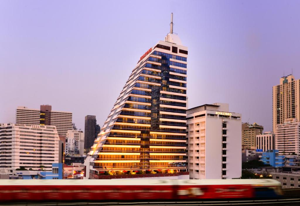 a tall building in a city with a red bus at Boulevard Hotel Bangkok Sukhumvit in Bangkok