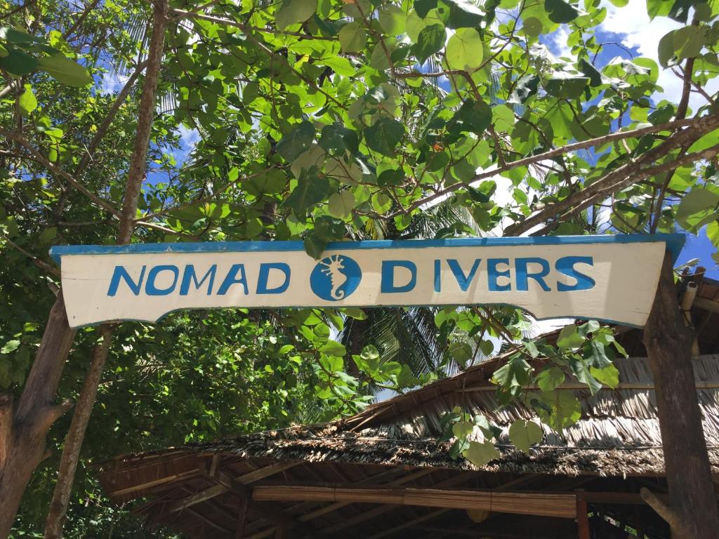 a sign that reads nomads and dingers hanging from a tree at Nomad Divers Bangka in Manado