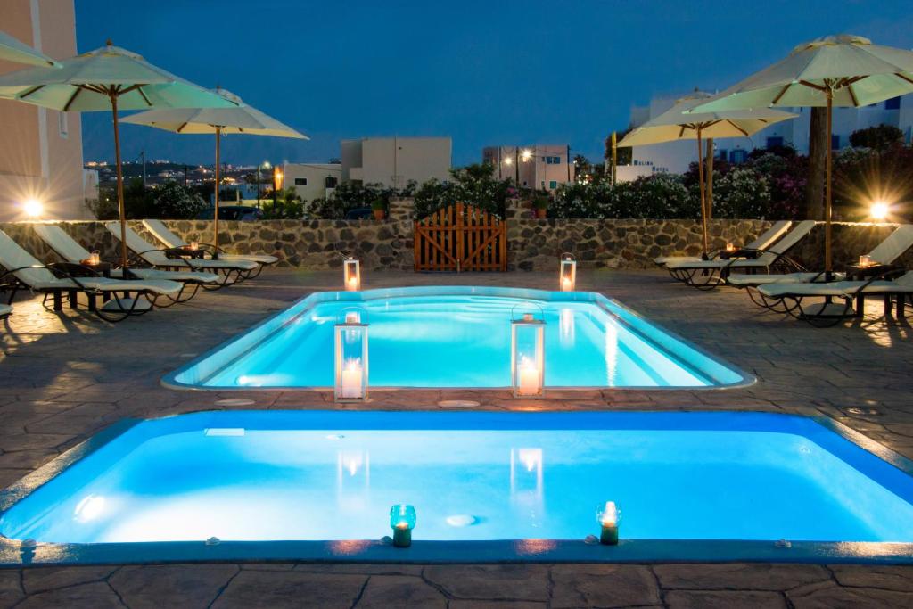 uma piscina à noite com mesas e guarda-sóis em Anessis em Fira
