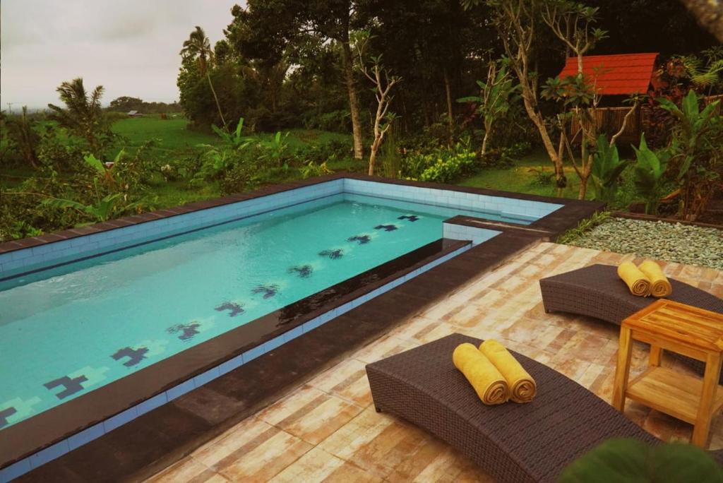 a swimming pool with two chairs and a table at Dukuh Baturan Villa in Jatiluwih