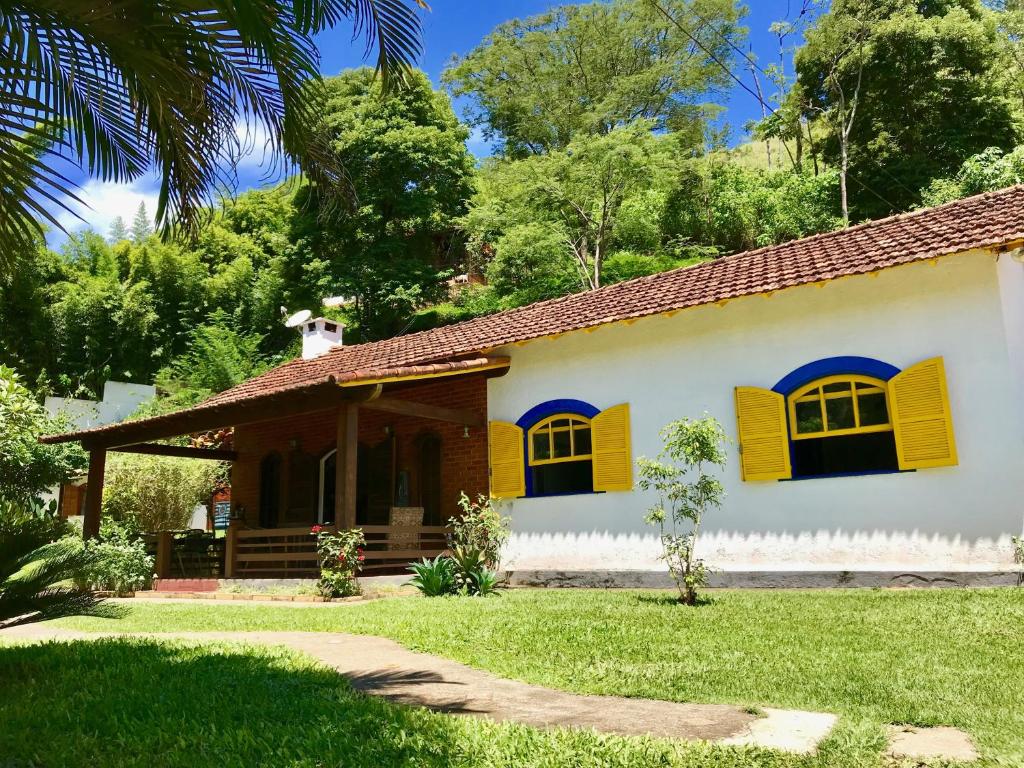 a house with yellow shuttered windows and a yard at Hostel 040 in Itaipava