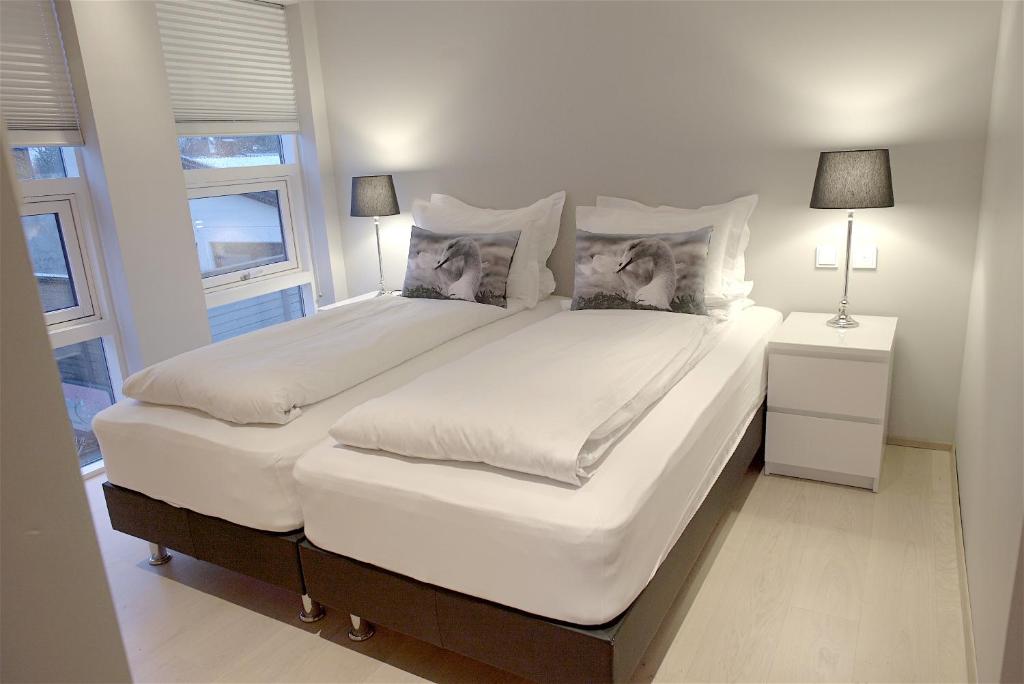 a large white bed in a bedroom with two windows at Om Apartments in Reykjavík