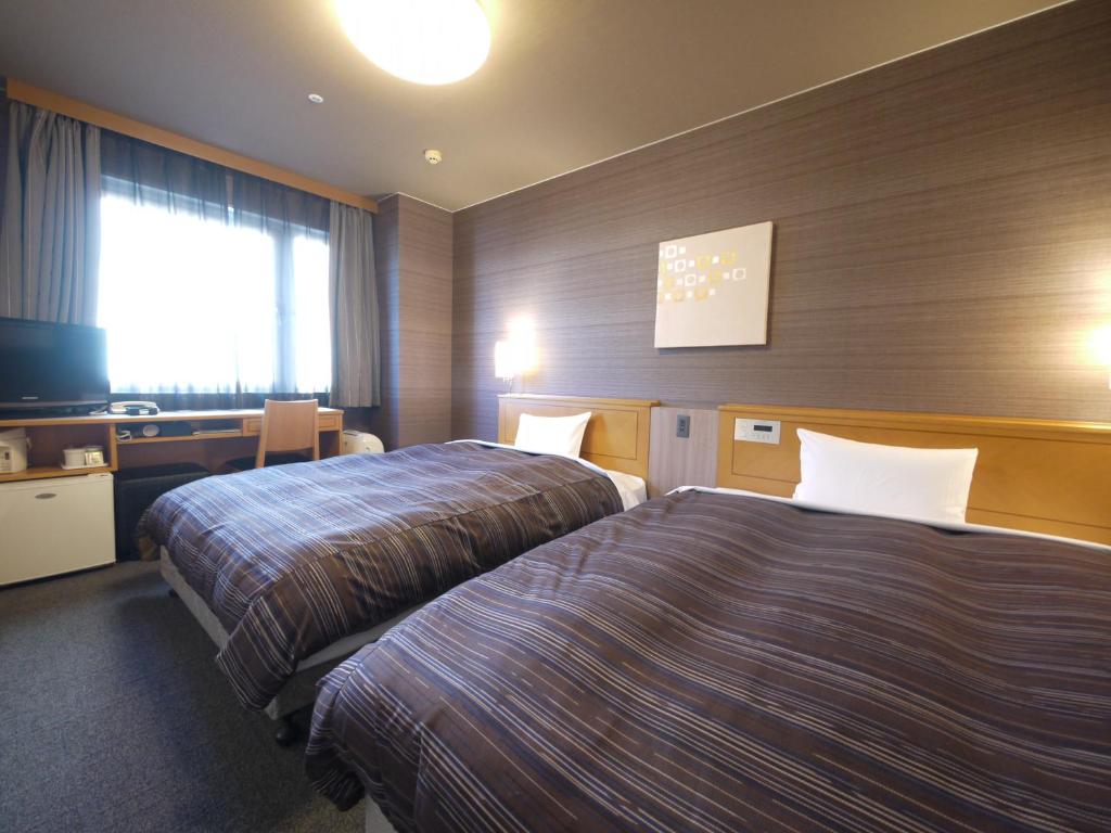 a hotel room with two beds and a television at Route Inn Grantia Komaki in Komaki