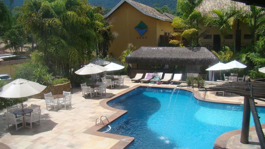 una piscina con mesas, sillas y sombrillas en Harmonia Flat Particular Ilhabela, en Ilhabela