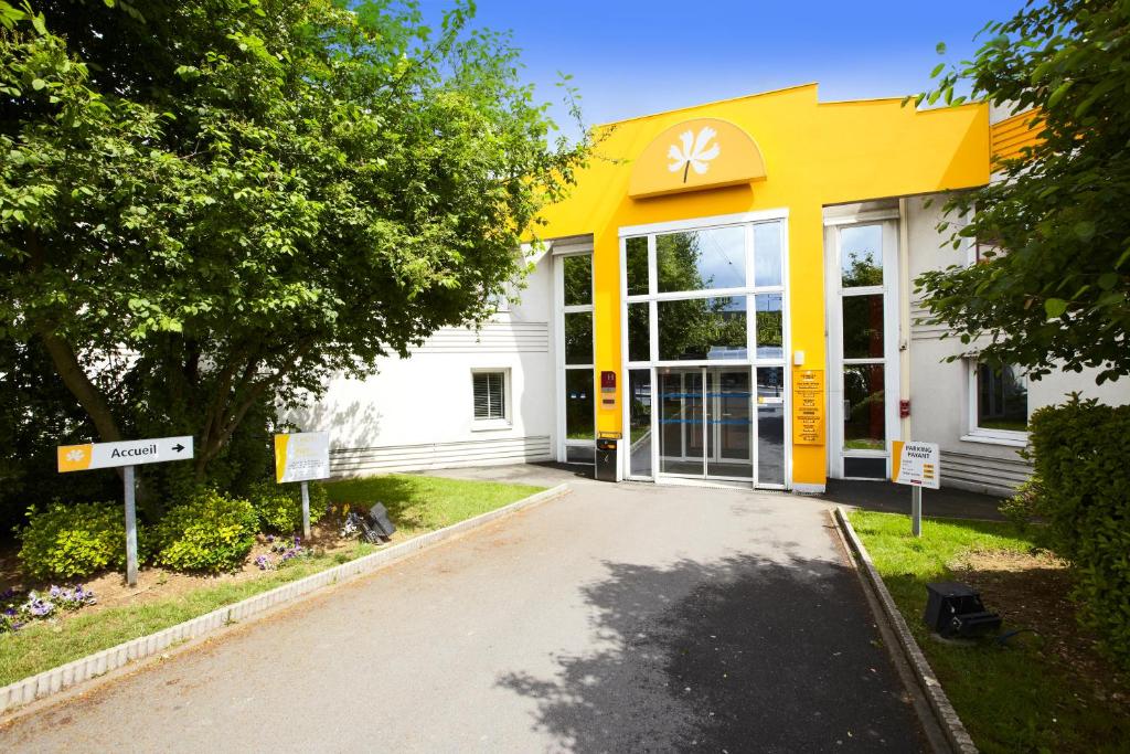 un bâtiment jaune et blanc avec un panneau devant lui dans l'établissement Premiere Classe Roissy CDG - Paris Nord 2 - Parc des Expositions, à Roissy-en-France