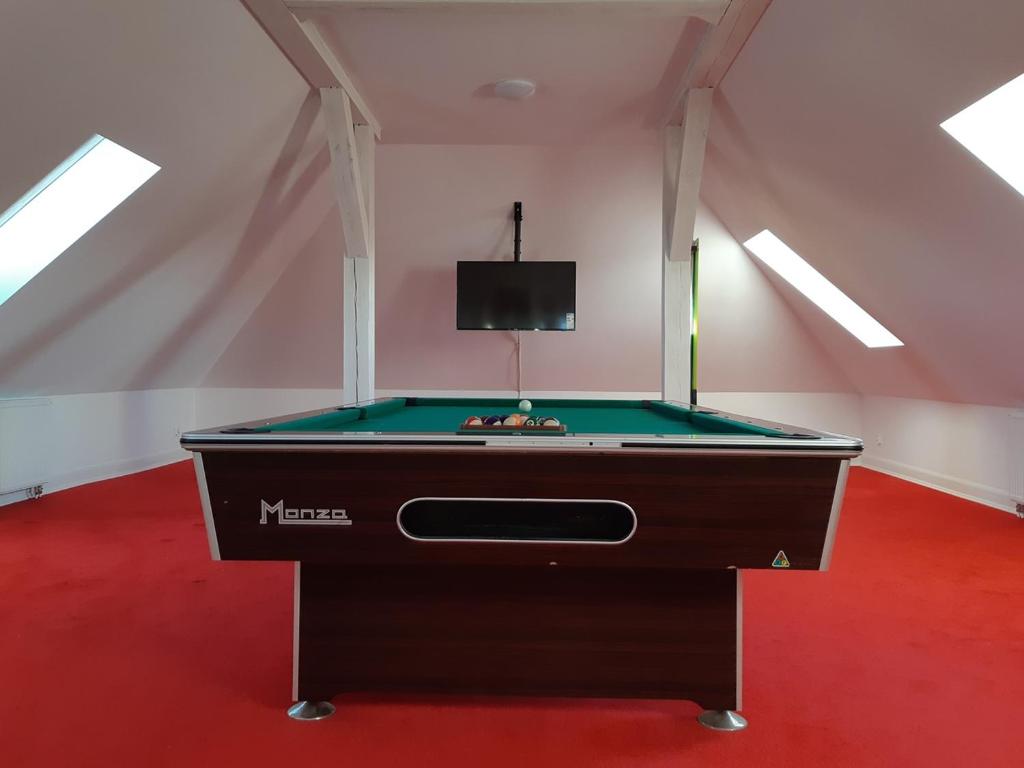 Pool table centered in bright attic room with wall-mounted TV and red carpeting throughout.