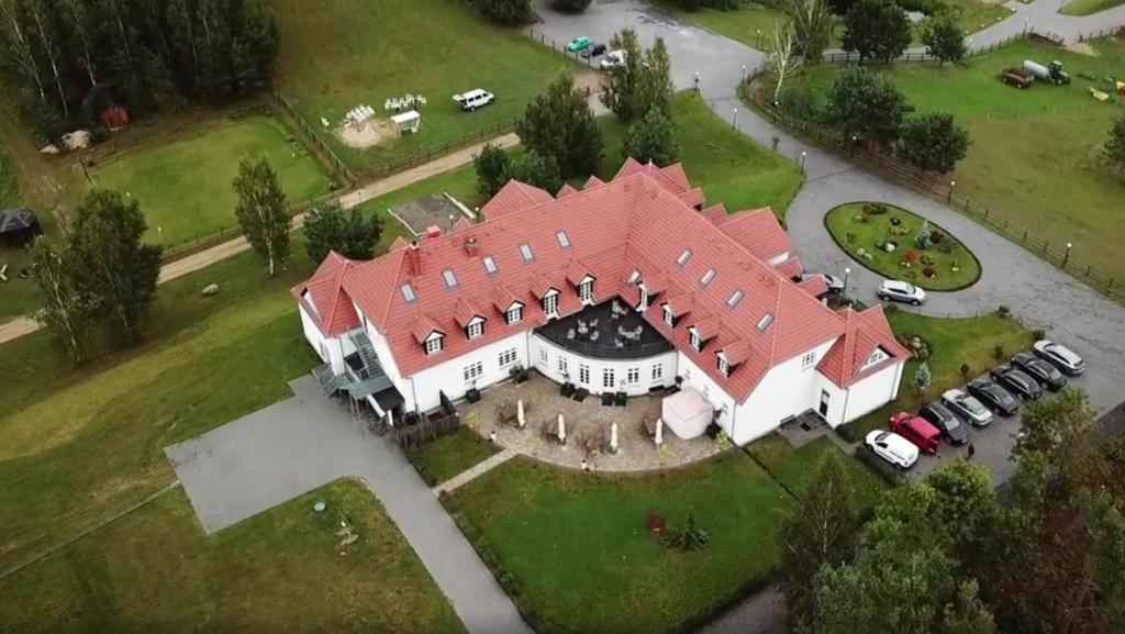Aerial view of a white manor with red roof, terrace, lawns and parked cars.