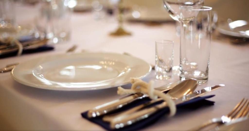 Close-up of elegant table setting with white plate, polished cutlery tied on navy napkin and glassware.