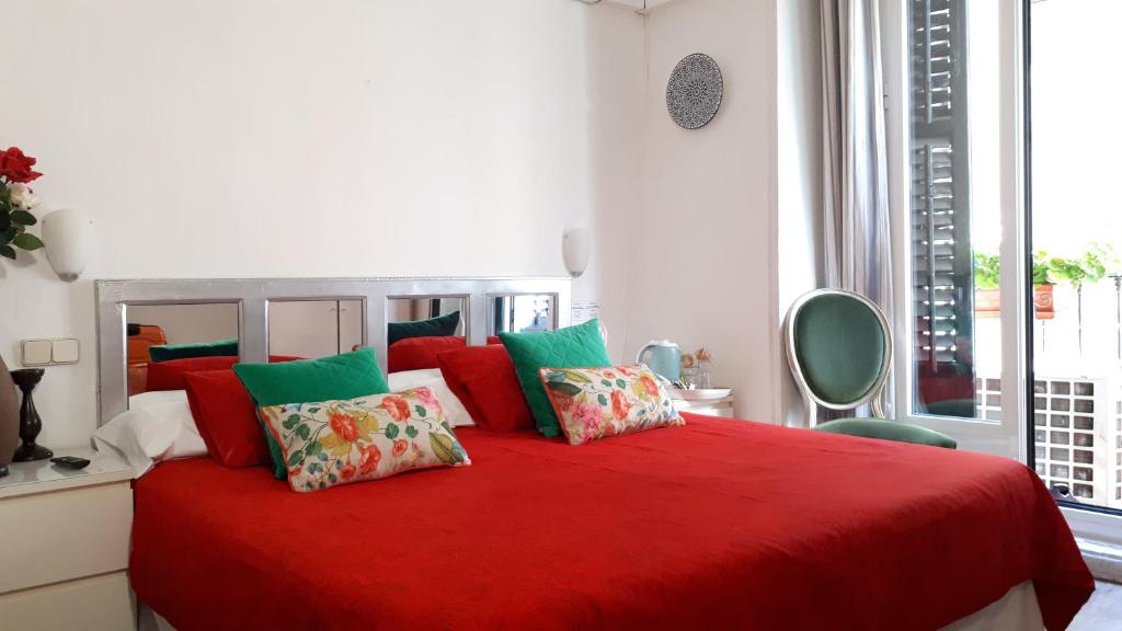 1 dormitorio con cama roja y almohadas coloridas en Hostal Casa Chueca, en Madrid