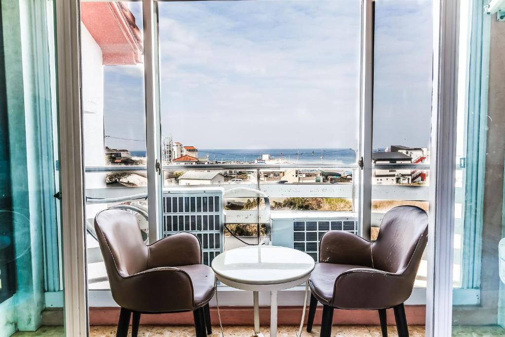 済州市にあるJeju Ocean Family Hotelの椅子2脚とテーブル、大きな窓が備わる客室です。