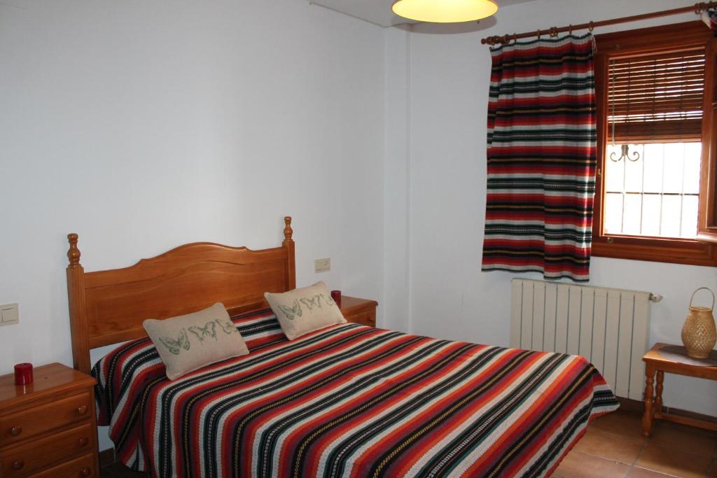 a bedroom with a bed with a striped blanket and a window at Apartamentos Rurales Rosendo: El Romero in Capileira