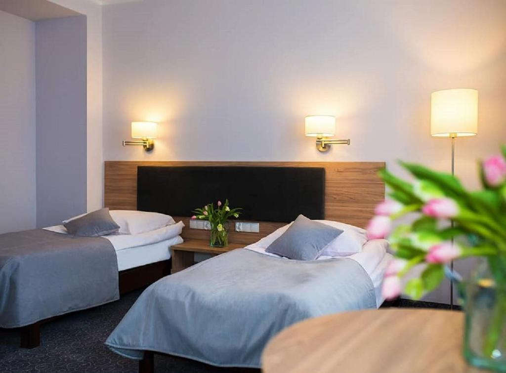 a hotel room with two beds and a table with flowers at Hotel Gromada in Koszalin