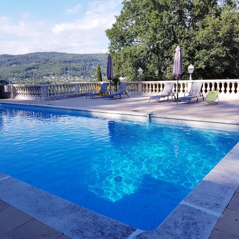 a blue swimming pool with chairs and umbrellas at Villa Manoe in Draguignan