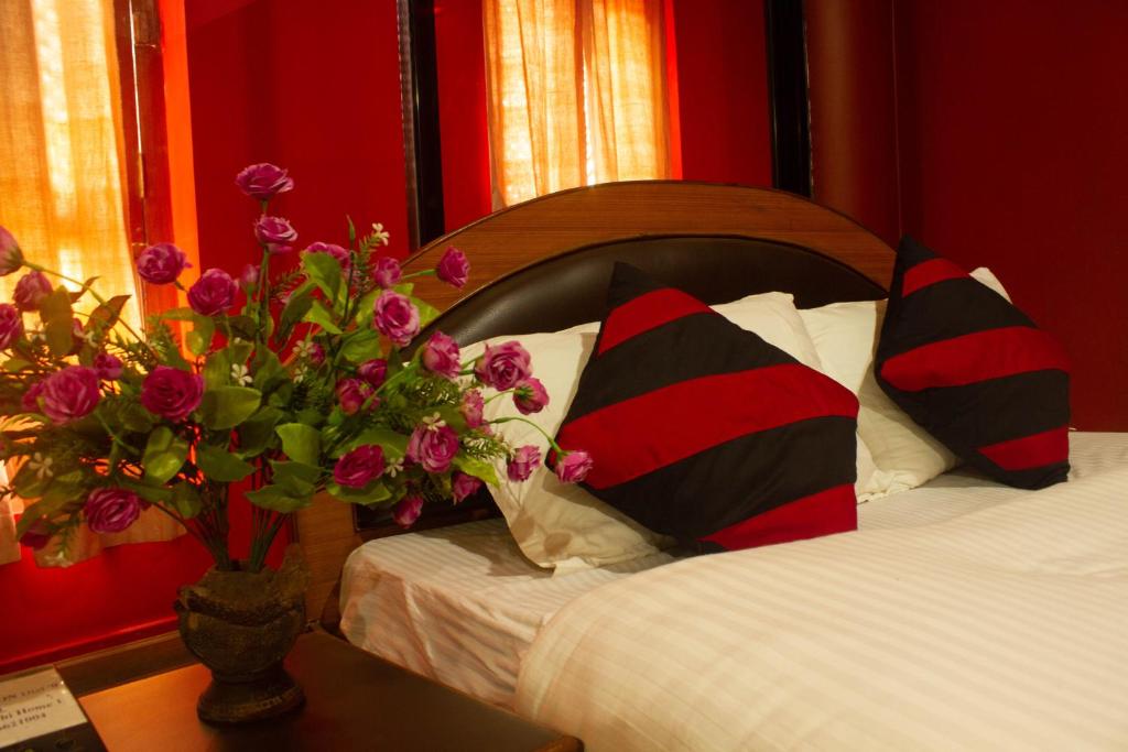 a bed with two pillows and a vase of flowers on a table at Siddhi Home & Restaurant in Bhaktapur