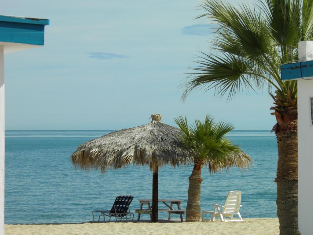 a beach with chairs and a straw umbrella and palm trees at #52 Bungalow Seaside Hotel & Victors RV Park in San Felipe