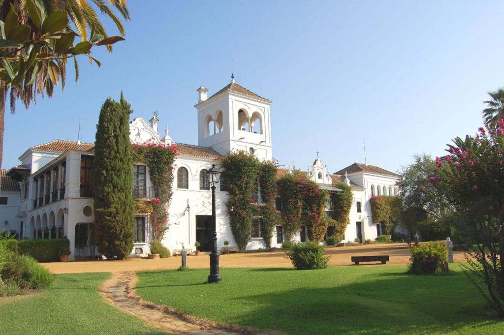 un gran edificio blanco con una torre de reloj en un parque en Hotel Cortijo El Esparragal, en Gerena