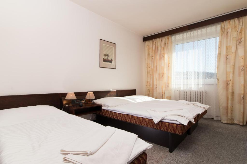 two beds in a hotel room with a window at Hotel Merkur - Jablonec nad Nisou in Jablonec nad Nisou