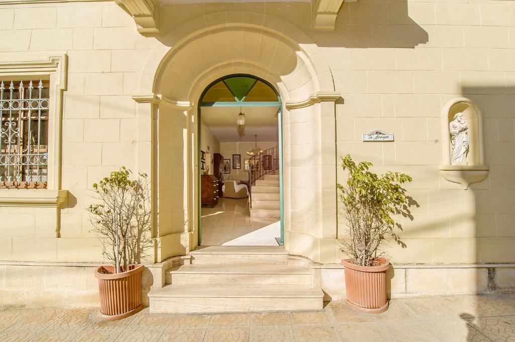 une entrée à un bâtiment avec deux plantes en pot dans l'établissement Ta Joseph, à Xewkija