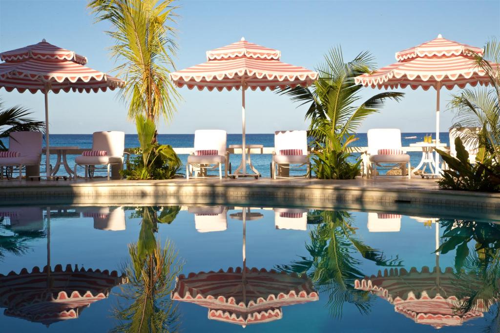 a swimming pool with umbrellas and chairs and the ocean at Cobblers Cove - Barbados in Saint Peter