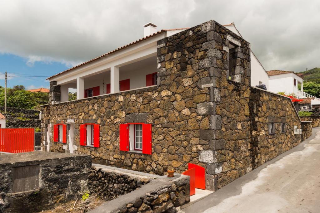 a stone house with red windows and a stone wall at Ilhéu do Areeiro in Madalena