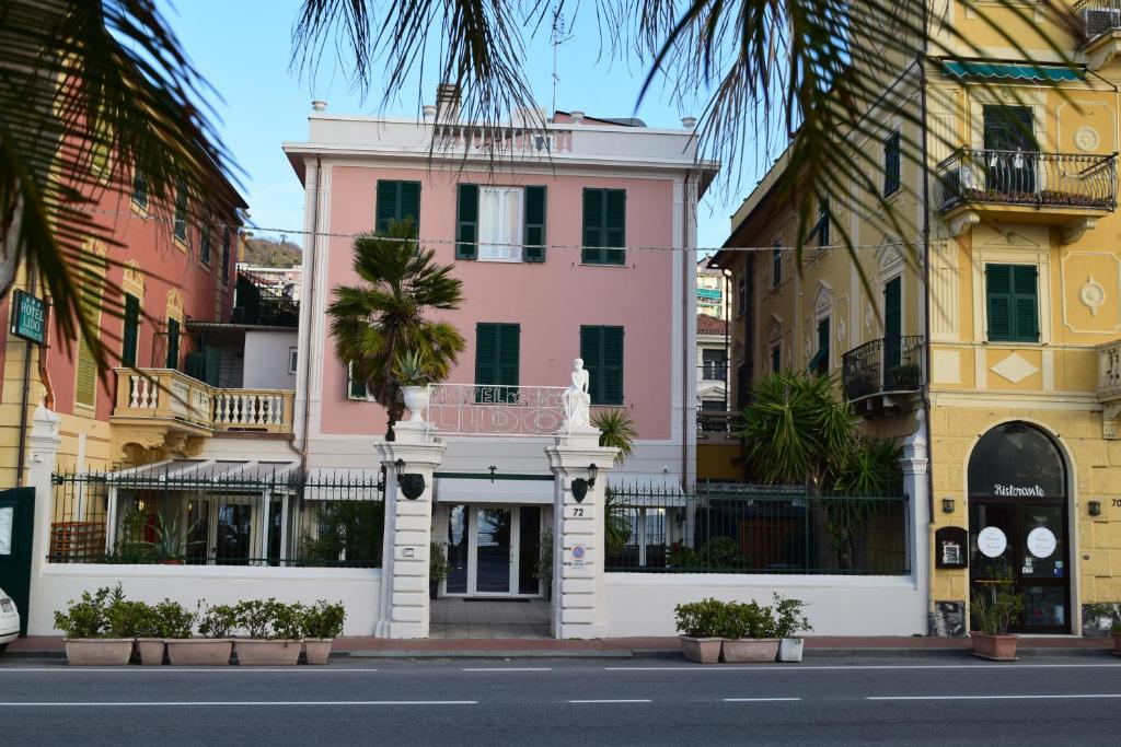 un edificio rosa en una calle de la ciudad con palmeras en Hotel Lido en Varazze