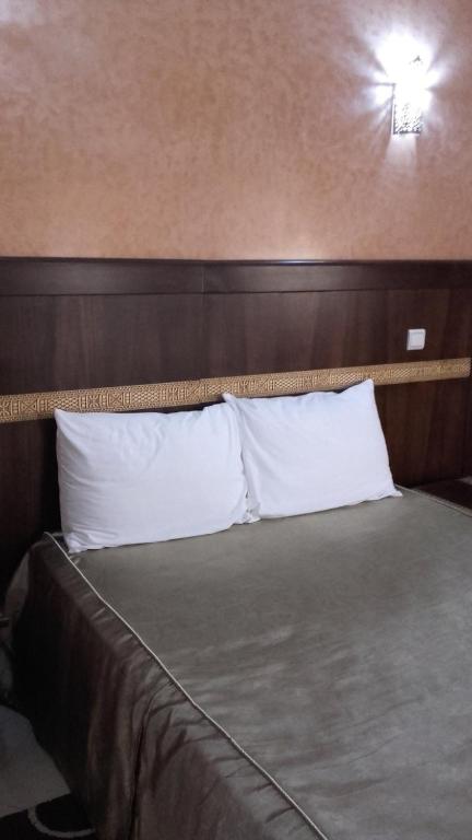 a bed with white pillows and a wooden headboard at Hotel AMOUDOU فندق أمودو in Tiznit