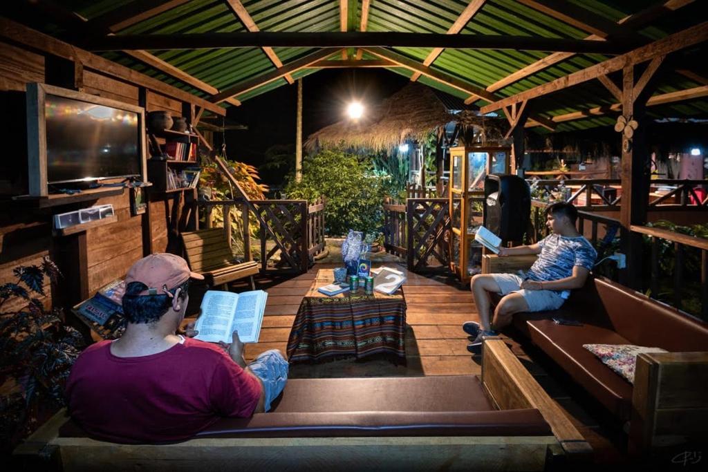 dos personas sentadas en un porche leyendo libros en Oro y Luna Lodge, en Carlos Julio Arosemena Tola