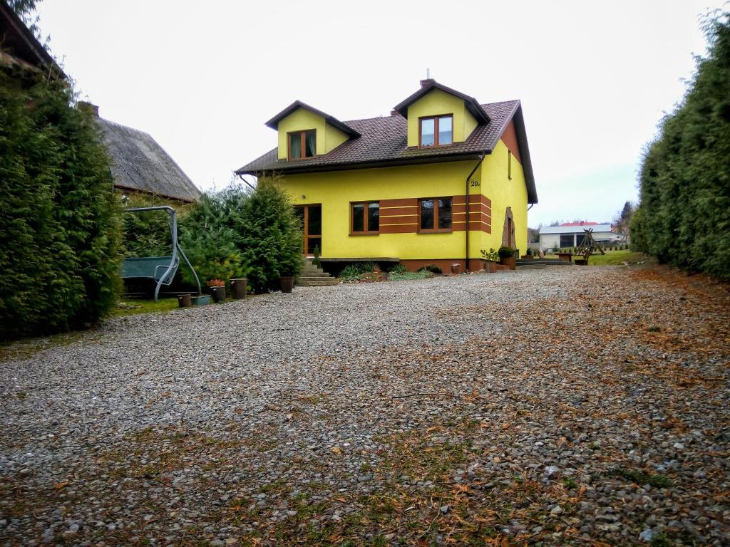 żółty dom z czarnym dachem na żwirowej drodze w obiekcie Pokoje na Wiejskiej w Nałęczowie