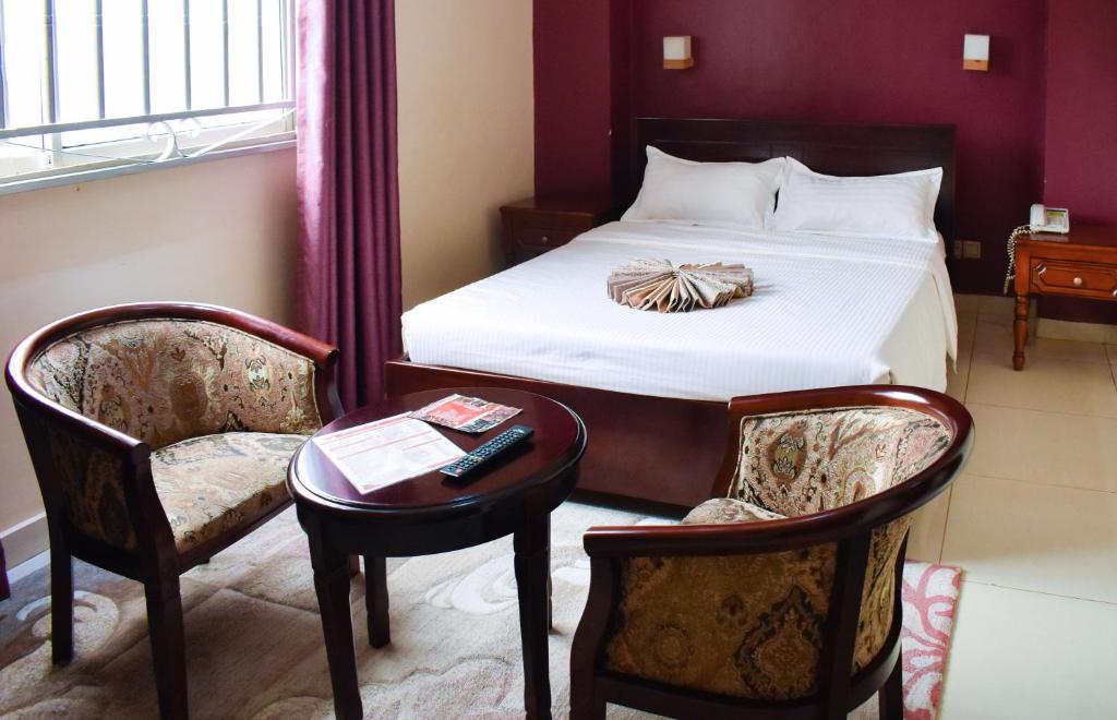 um quarto com uma cama, 2 cadeiras e uma mesa em Diamonds Hotel Kampala em Kampala