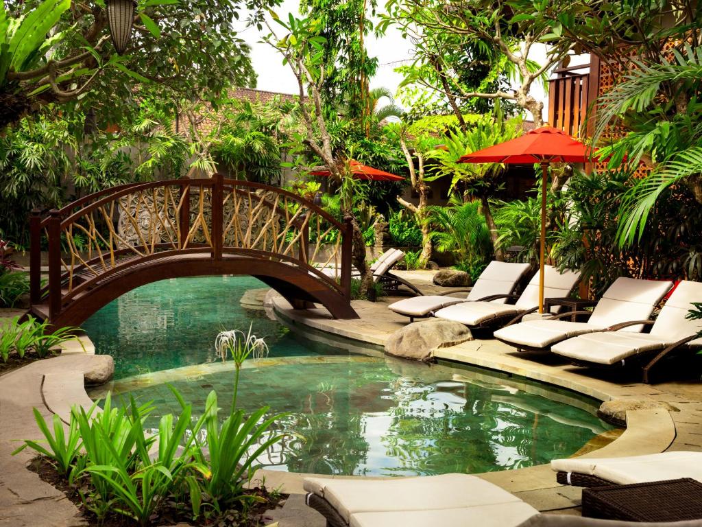 eine Brücke über einen Pool in einem Garten mit Liegestühlen in der Unterkunft Adiwana Monkey Forest in Ubud