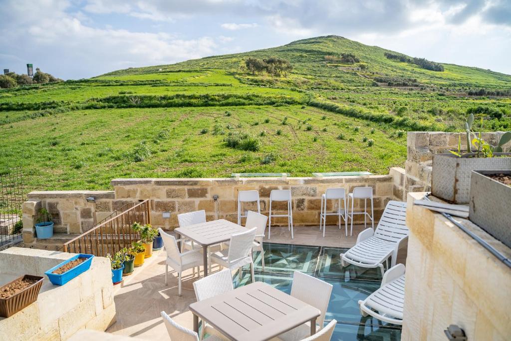 un patio con mesas, sillas y una colina en Ta Pinu Guesthouse en Għarb